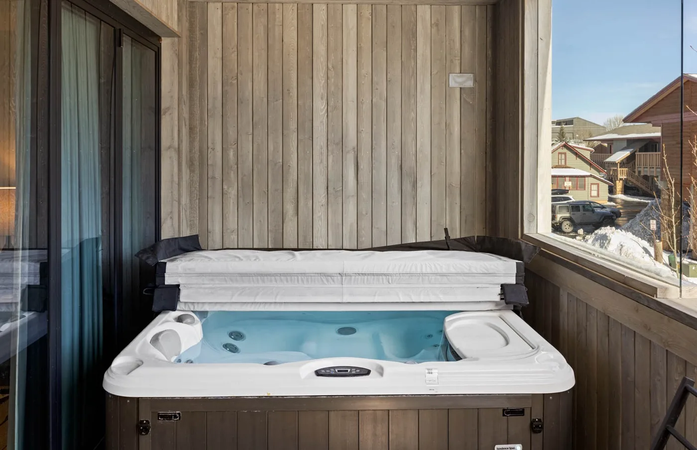 An indoor hot tub sits beneath a wooden wall beside large windows.