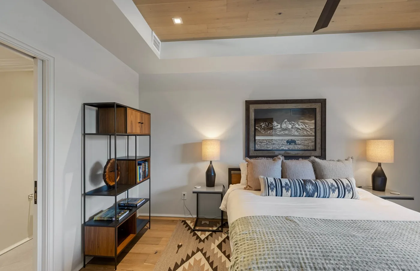 A bedroom with a neatly made bed, bedside lamps, and a patterned rug.