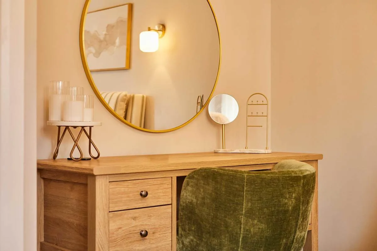 A wooden dressing table with a round mirror and a green upholstered seat.