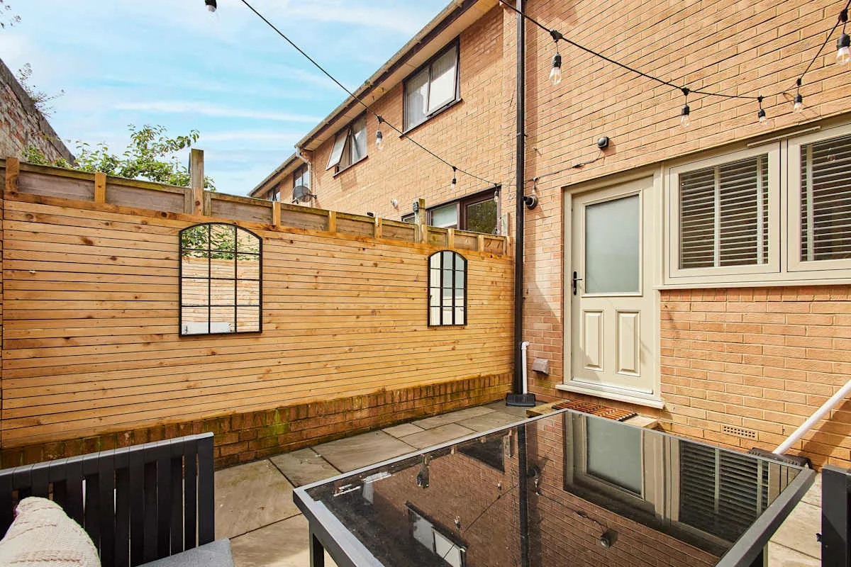 A paved brick patio with a wooden privacy fence and string lights.