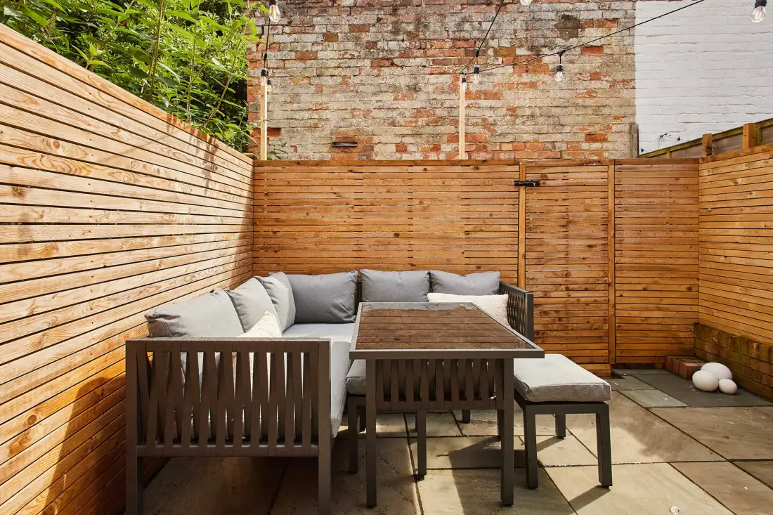 An outdoor patio has wooden privacy fencing and a table with seating.