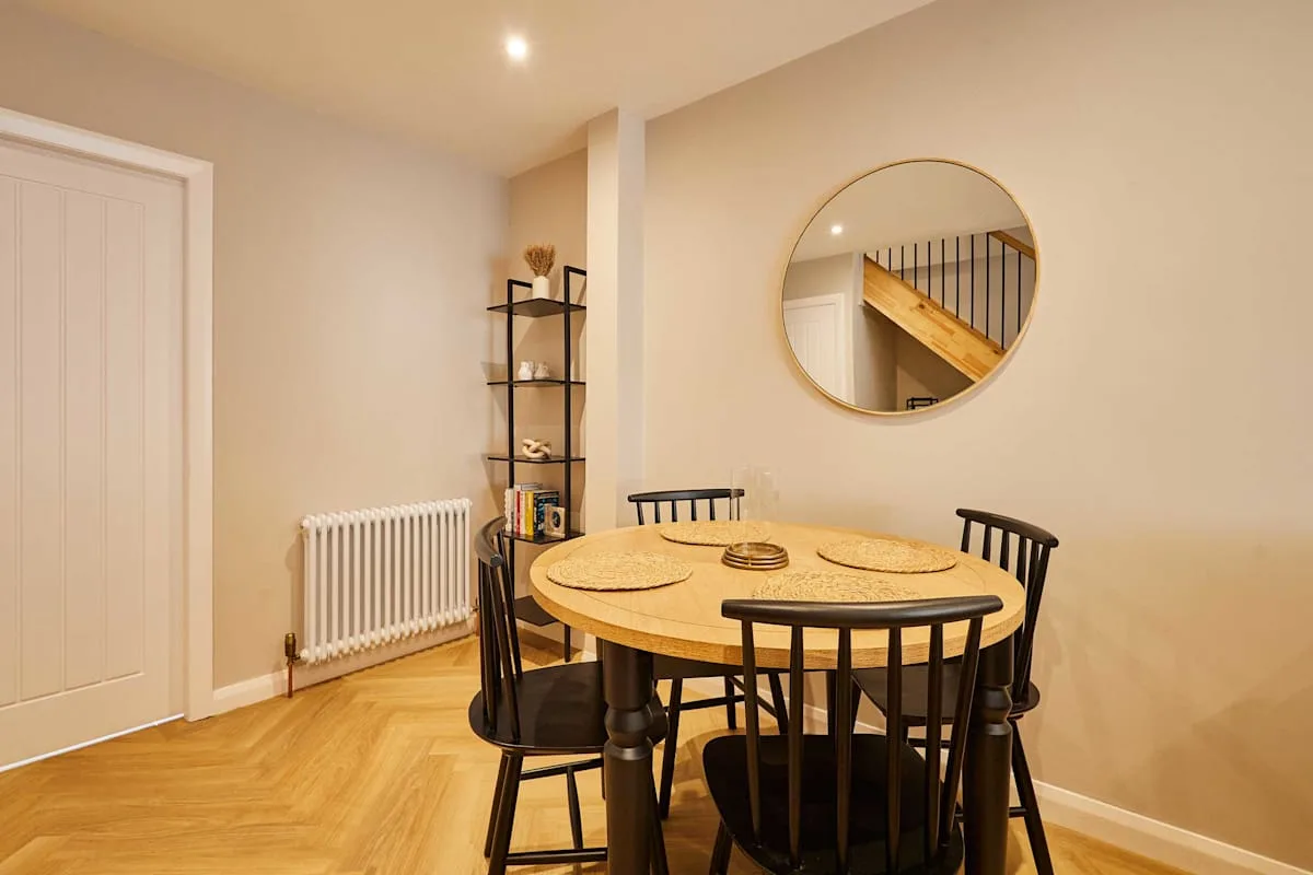A dining area with a round table and chairs beneath a circular wall mirror.