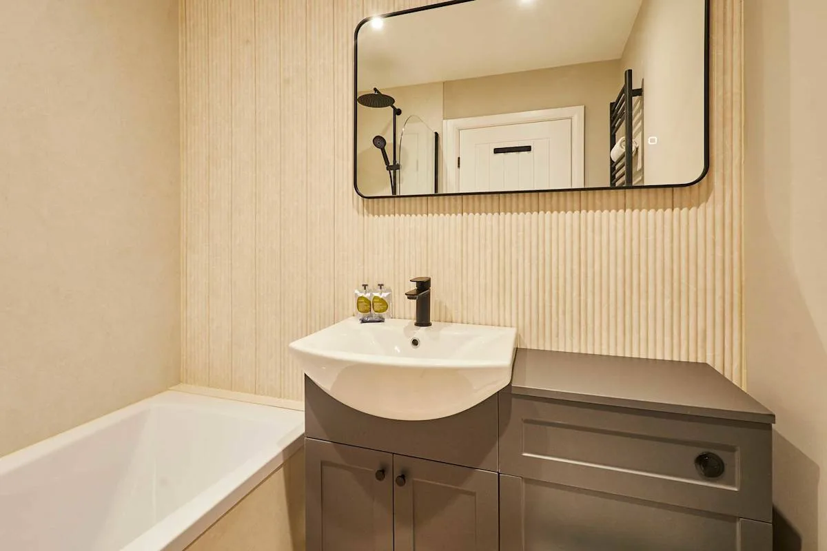 A bathroom with a bathtub, sink, and large wall mirror.