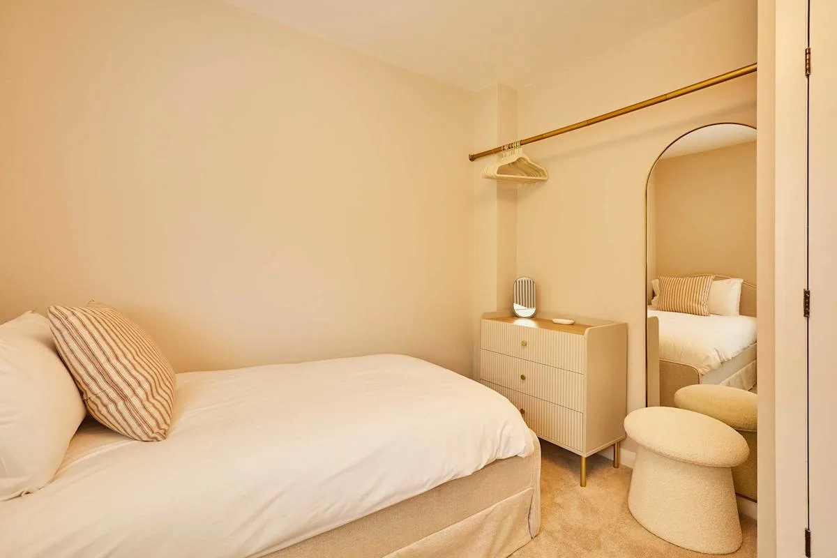 A bedroom with a bed, a dresser, and a full-length mirror.