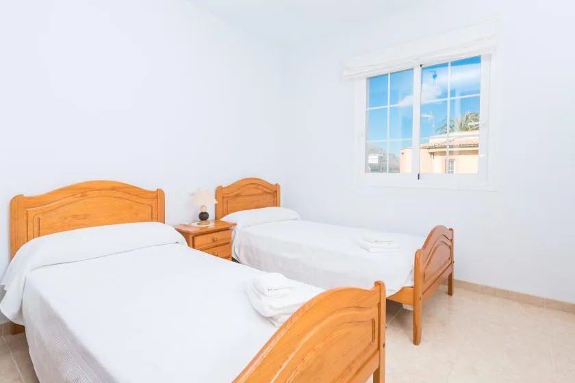 A bright bedroom with two wooden beds beneath a large window.