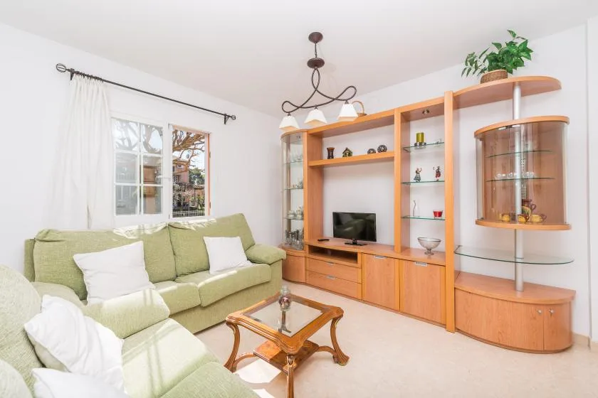 A bright living room with green seating, a television, and built-in shelving.