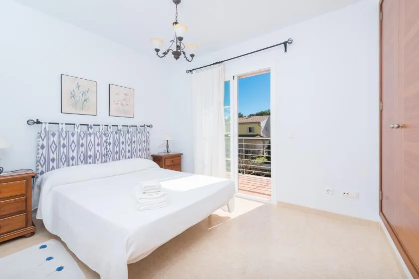 A bright bedroom with a white bed and an open balcony doorway.