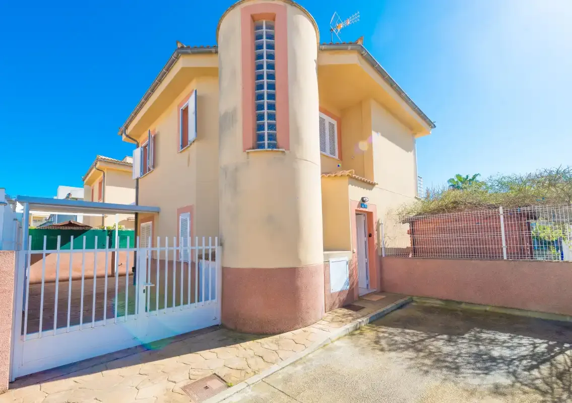 A yellow two-story house stands behind a white metal gate.