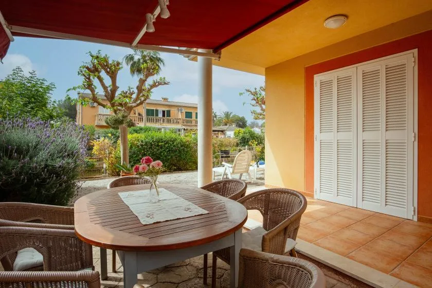A covered patio with a round table and wicker seating overlooks a garden.