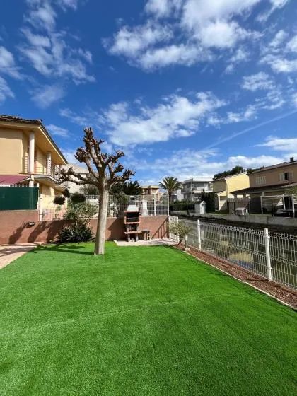 A green lawn fills an outdoor yard beside a fenced patio and houses.