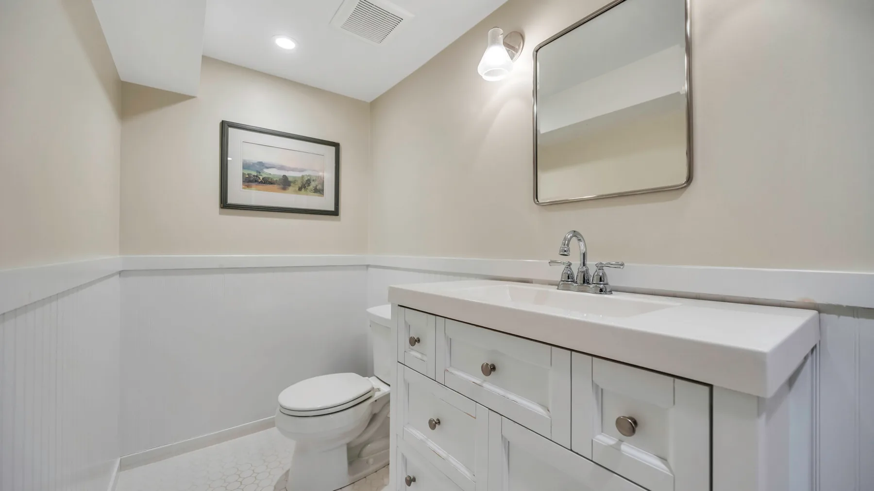 A bathroom with a toilet, sink, and wall mirror.