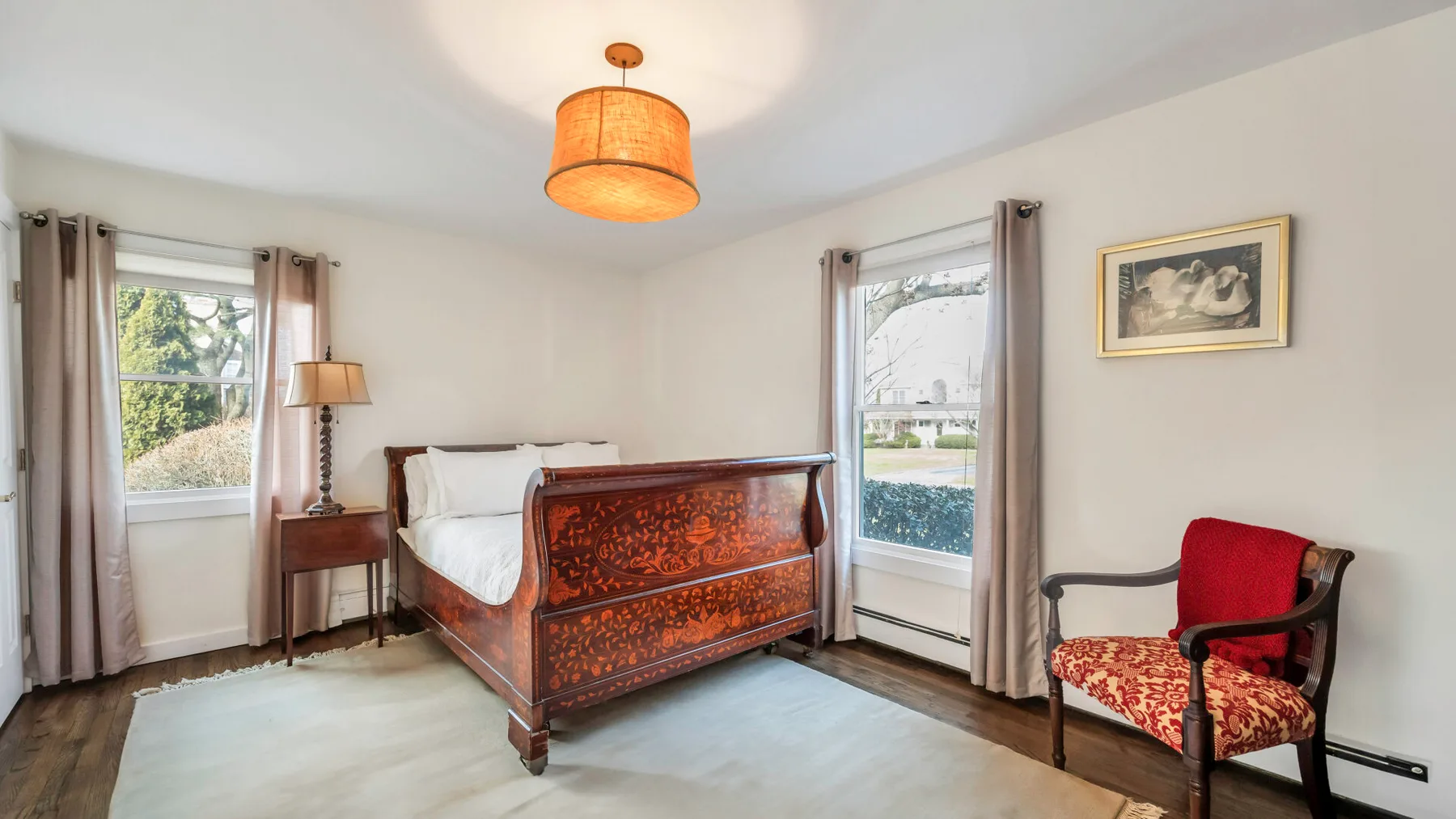 A bedroom with an ornate wooden bed between two windows.