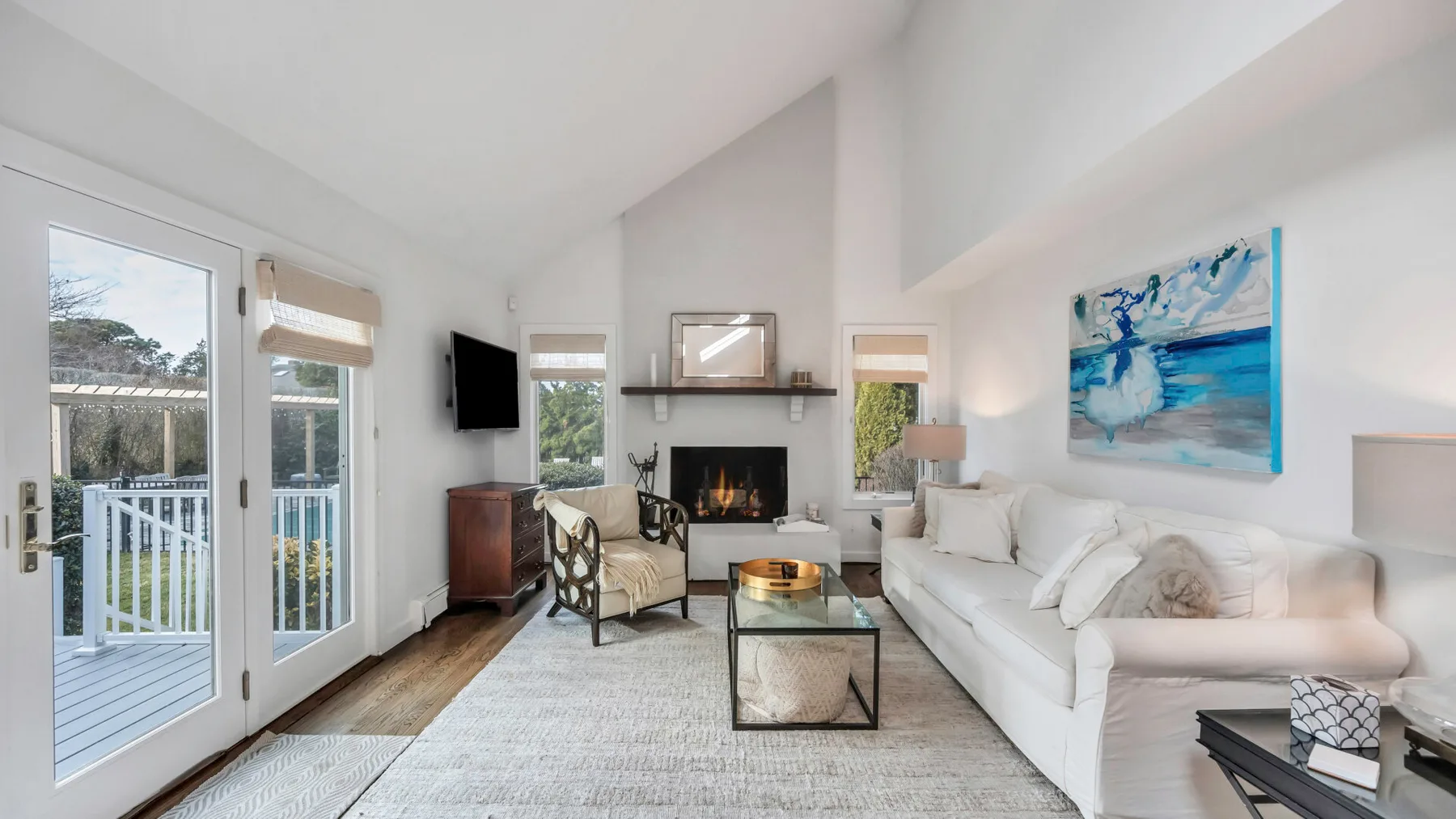 A bright living room with a white sofa, fireplace, and large windows.