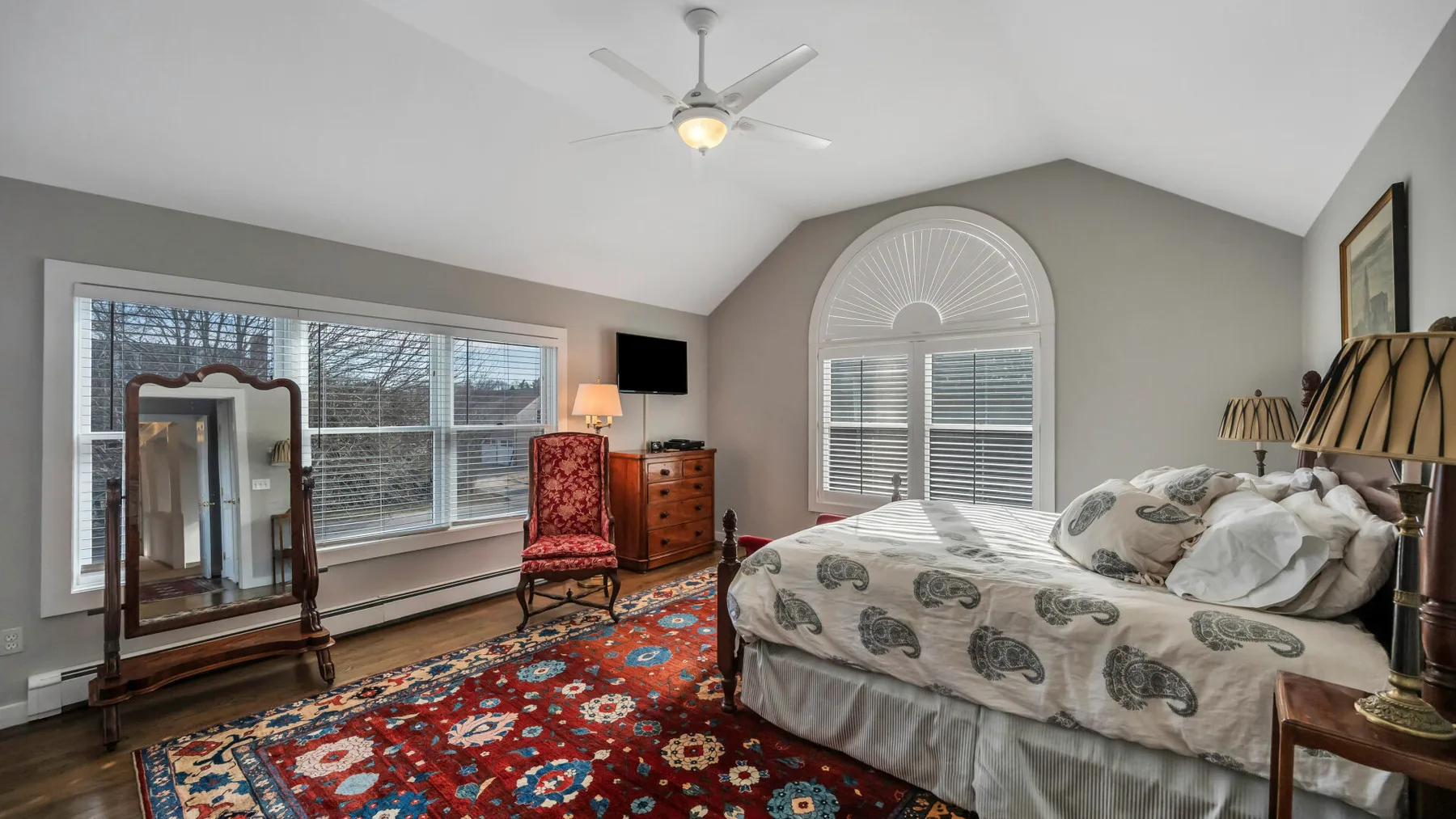 A bedroom with a bed, patterned rug, and windows along the wall.
