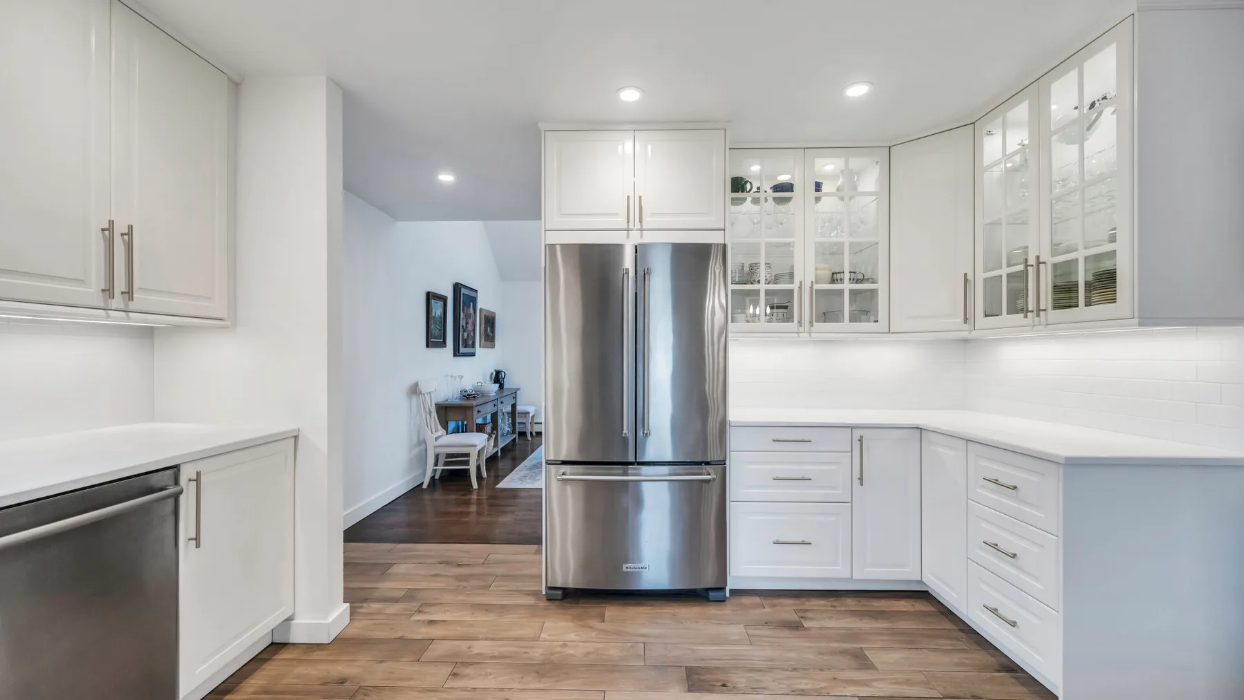 A bright white kitchen with stainless steel appliances and wood flooring.