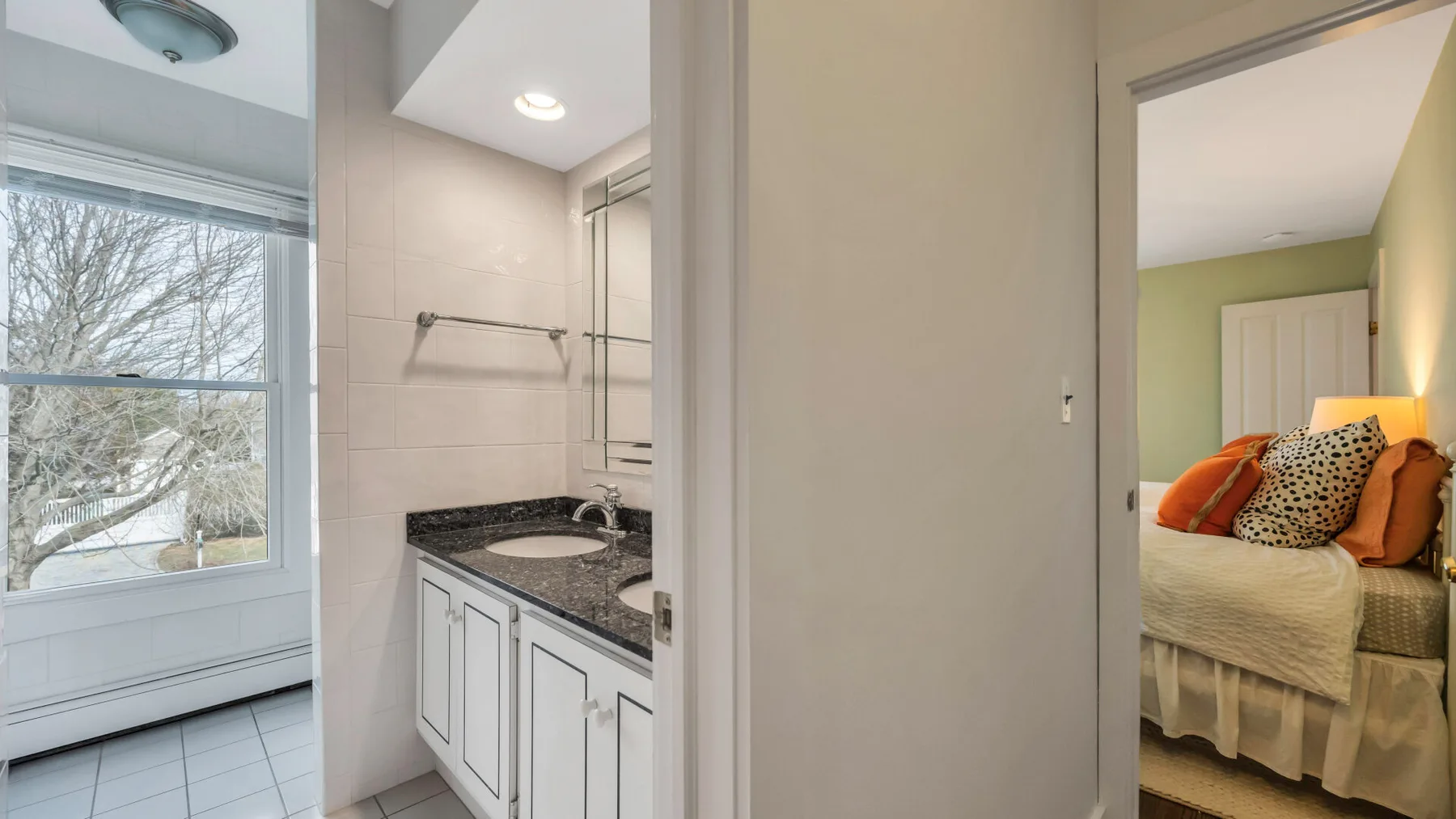 A bathroom vanity and shower area opens onto a bedroom with a bed.