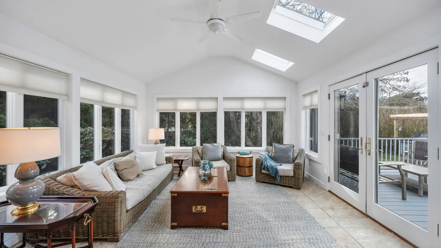 A bright sunroom with seating arranged around a central coffee table and wide windows.