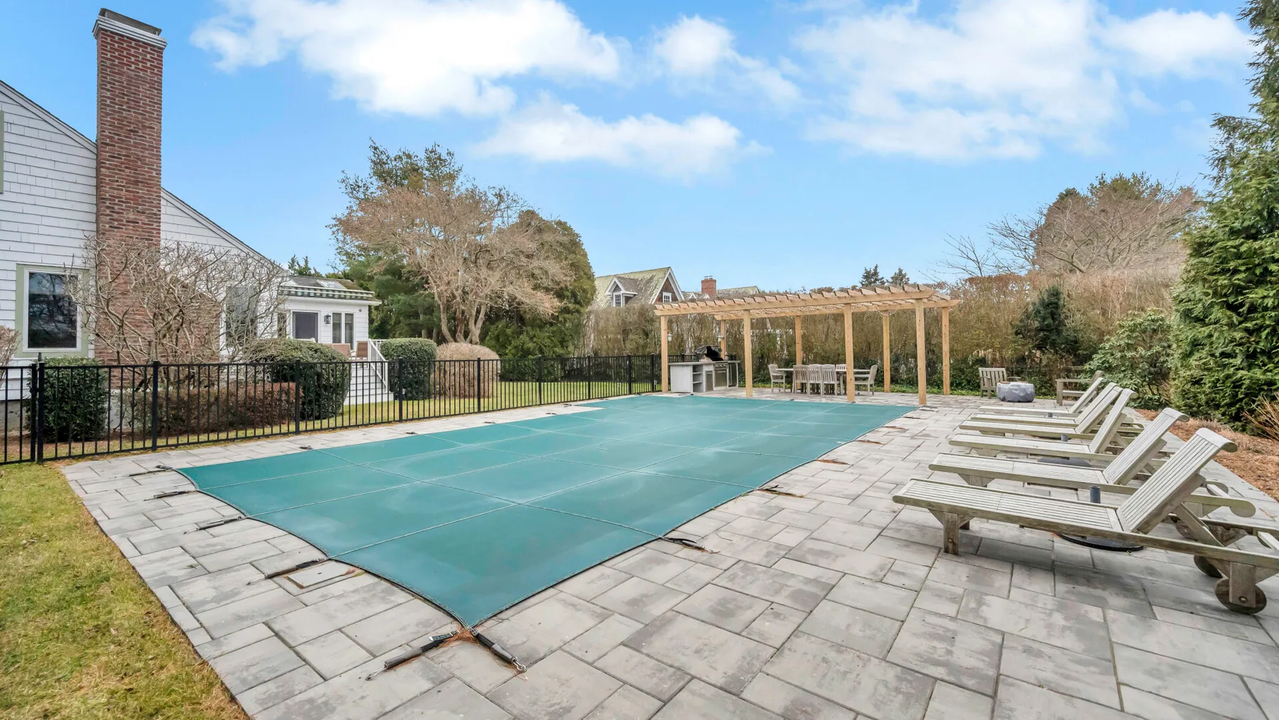 An outdoor swimming pool sits beside a paved patio with lounge seating.