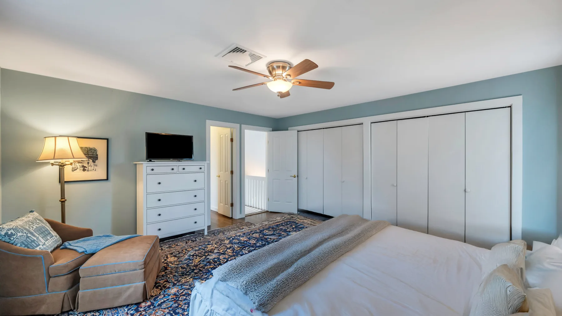 A bedroom with a bed, dresser, and seating beside a patterned rug.