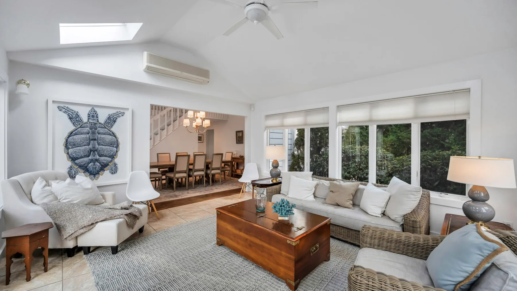 A bright living room with seating, a wooden coffee table, and wide windows.