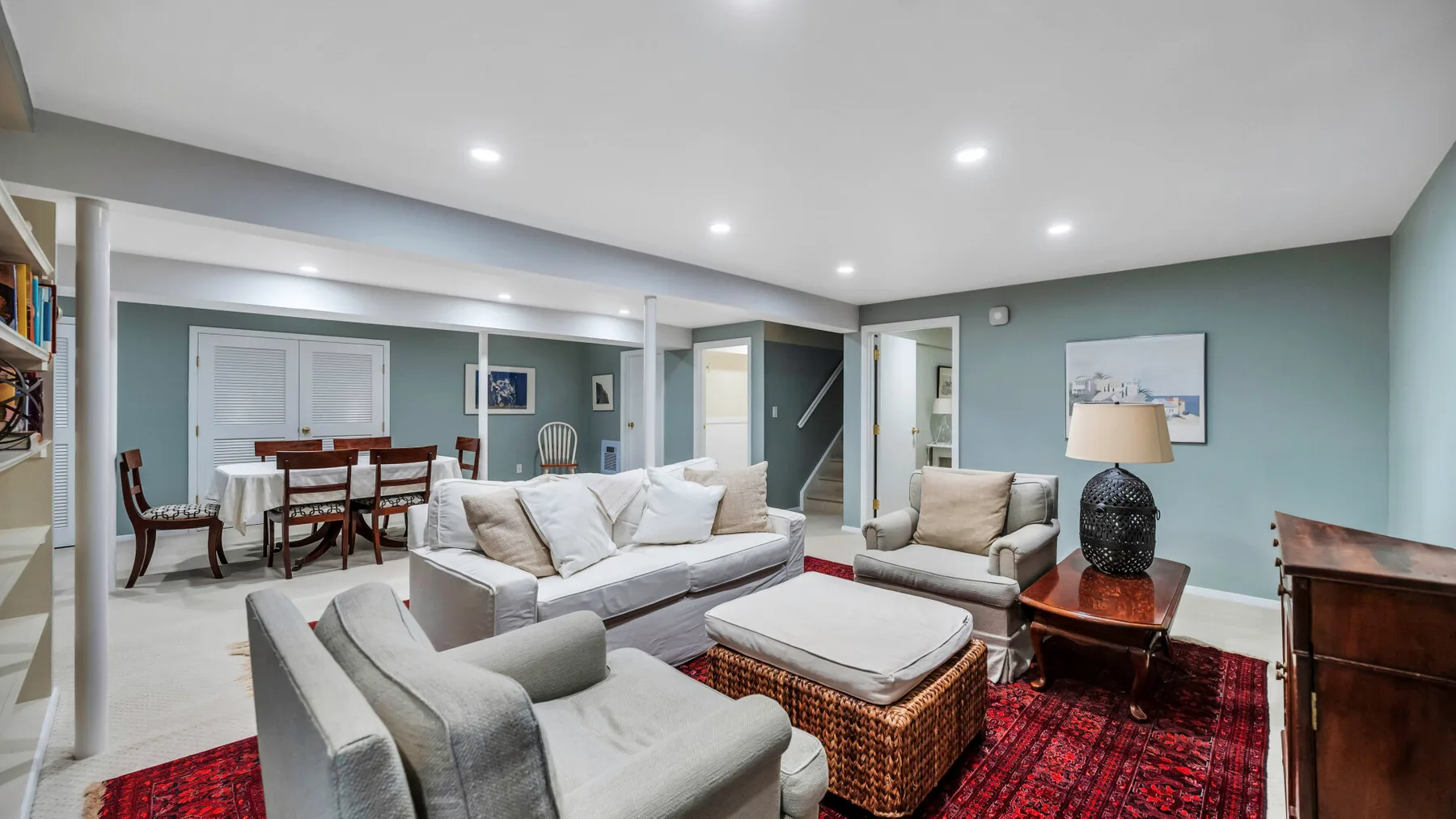 A living room with light seating, a red rug, and a dining area.