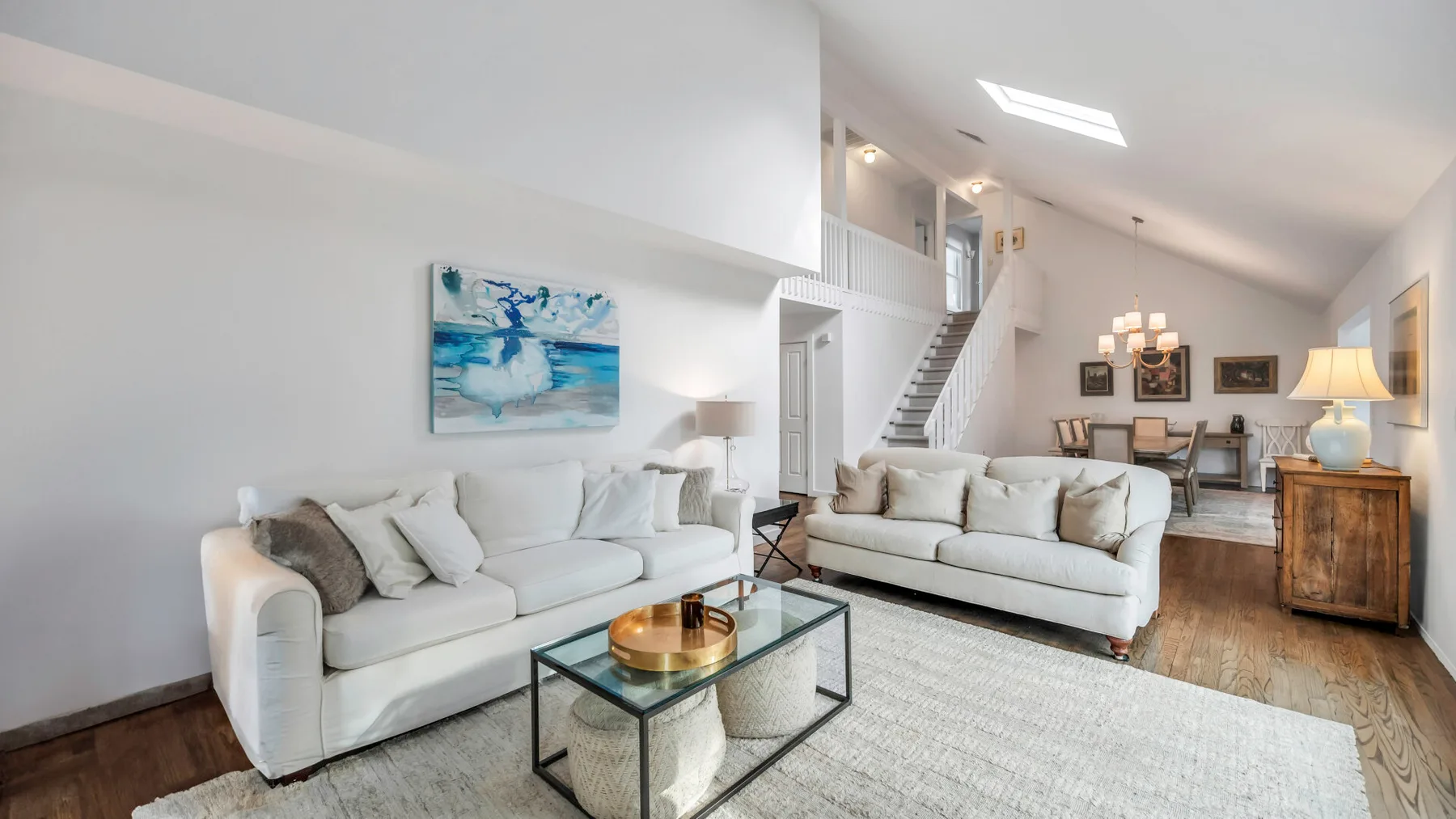 A bright living room with light-colored seating and a glass coffee table.