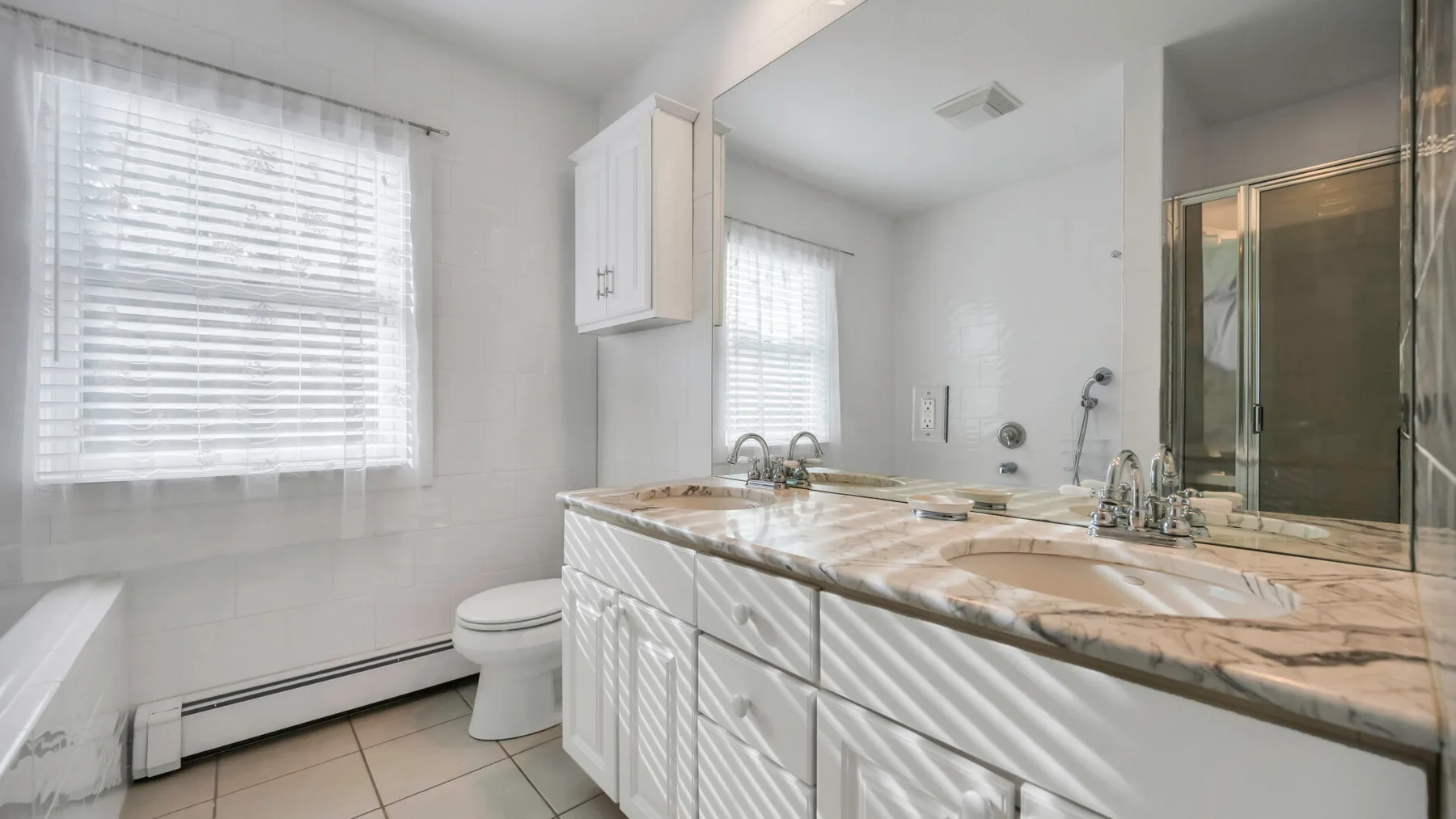 A bright bathroom with a long vanity, sinks, and a large window.
