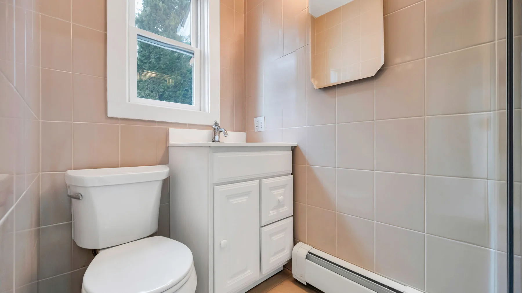 A tiled bathroom with a toilet, vanity, and window.