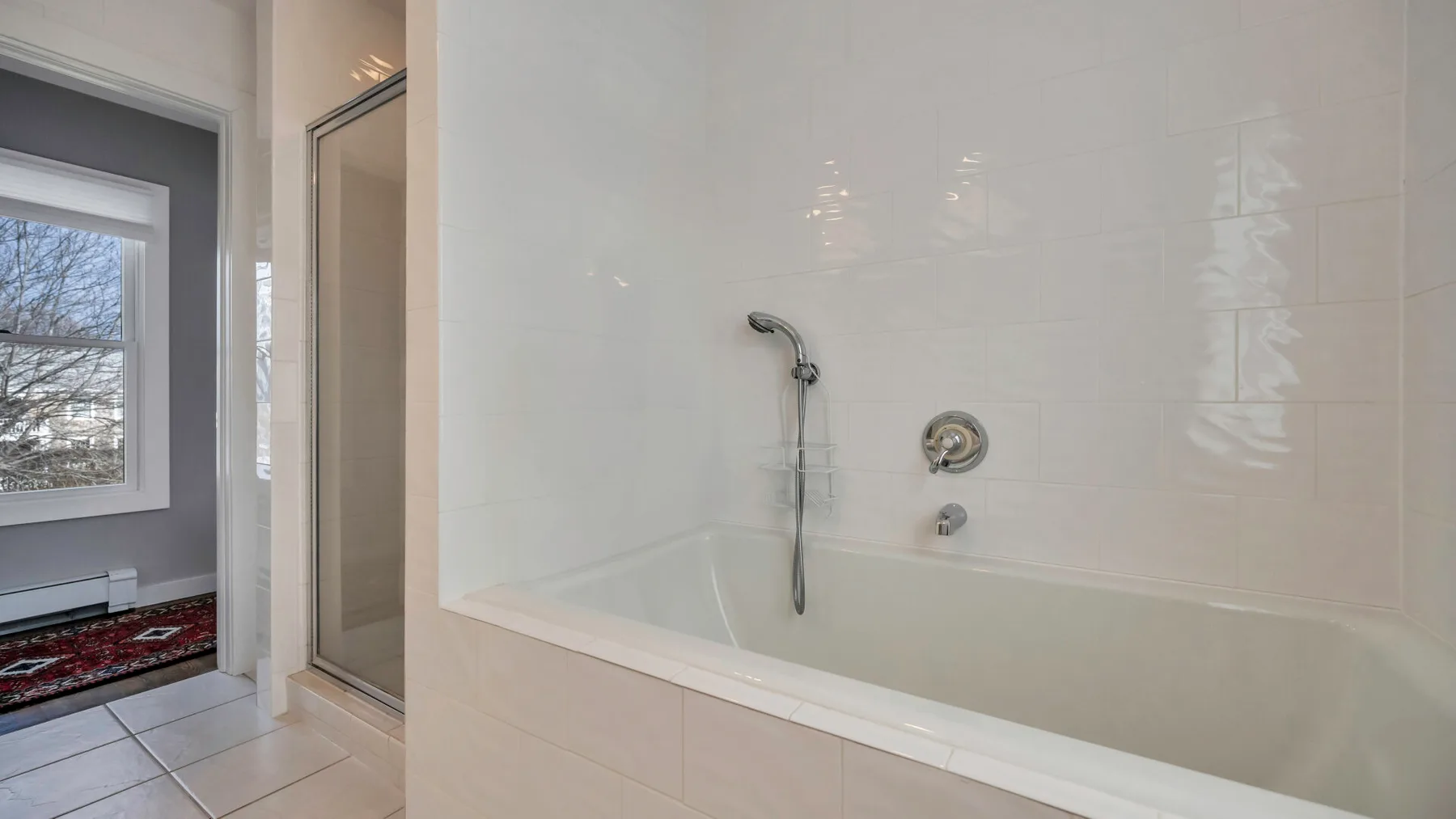 A tiled bathroom with a bathtub and handheld shower beside a window.