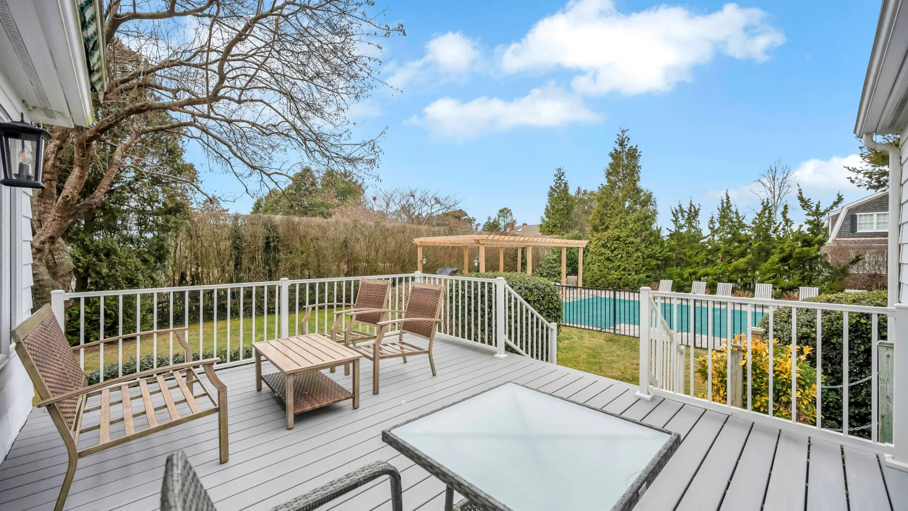 A raised outdoor deck with patio seating overlooks a swimming pool and landscaped yard.