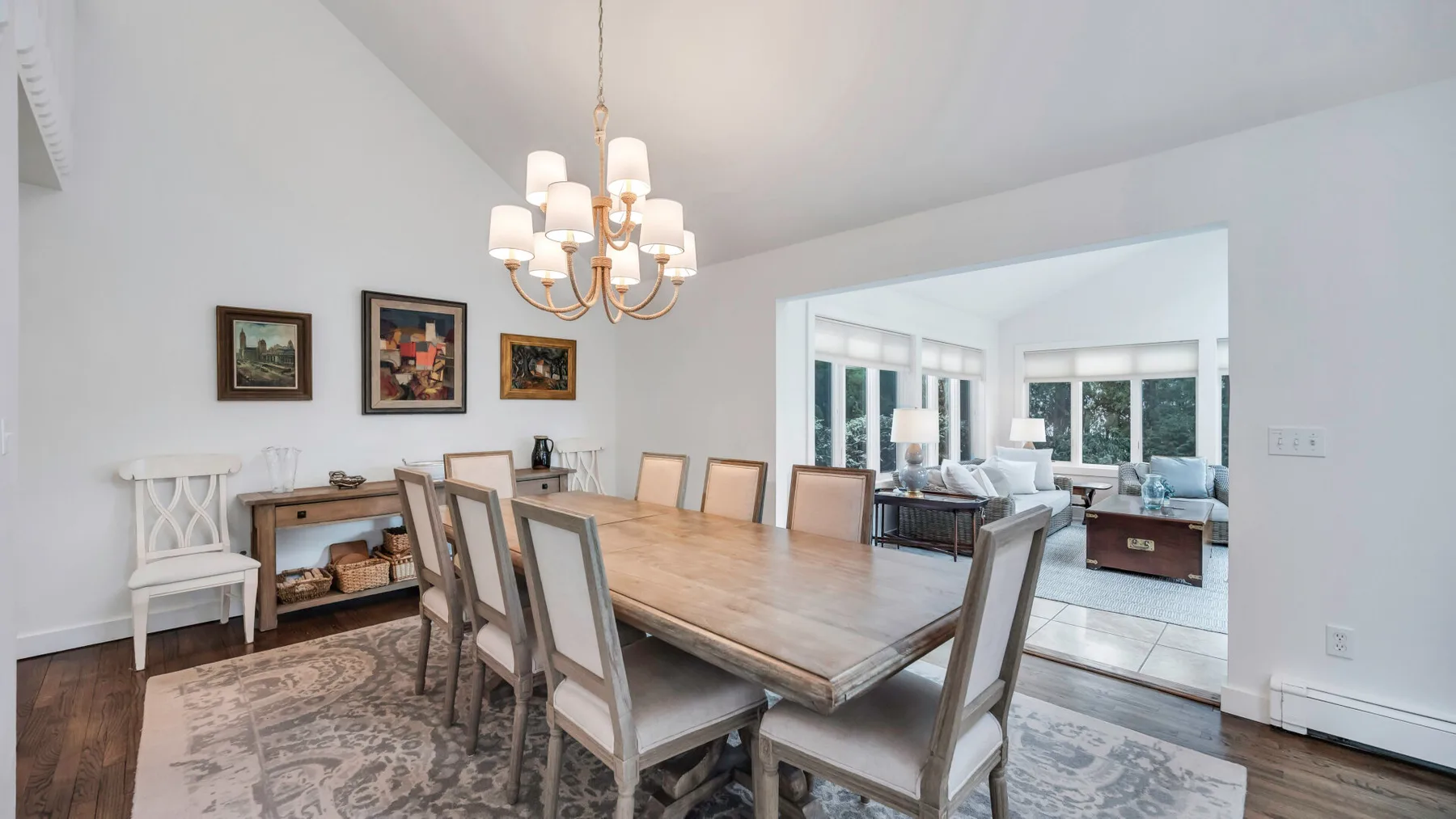A dining area with a long table and chandelier opens into a living room.