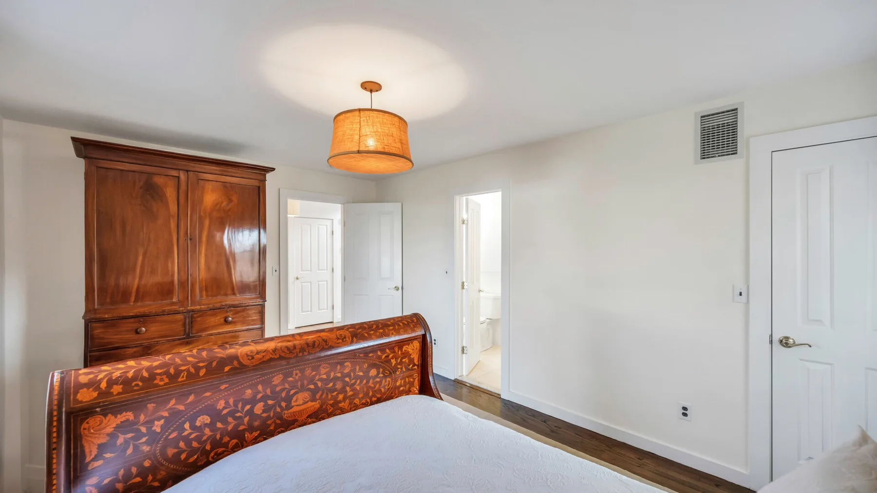A bedroom with a carved wooden bed, a wardrobe, and a hanging light.