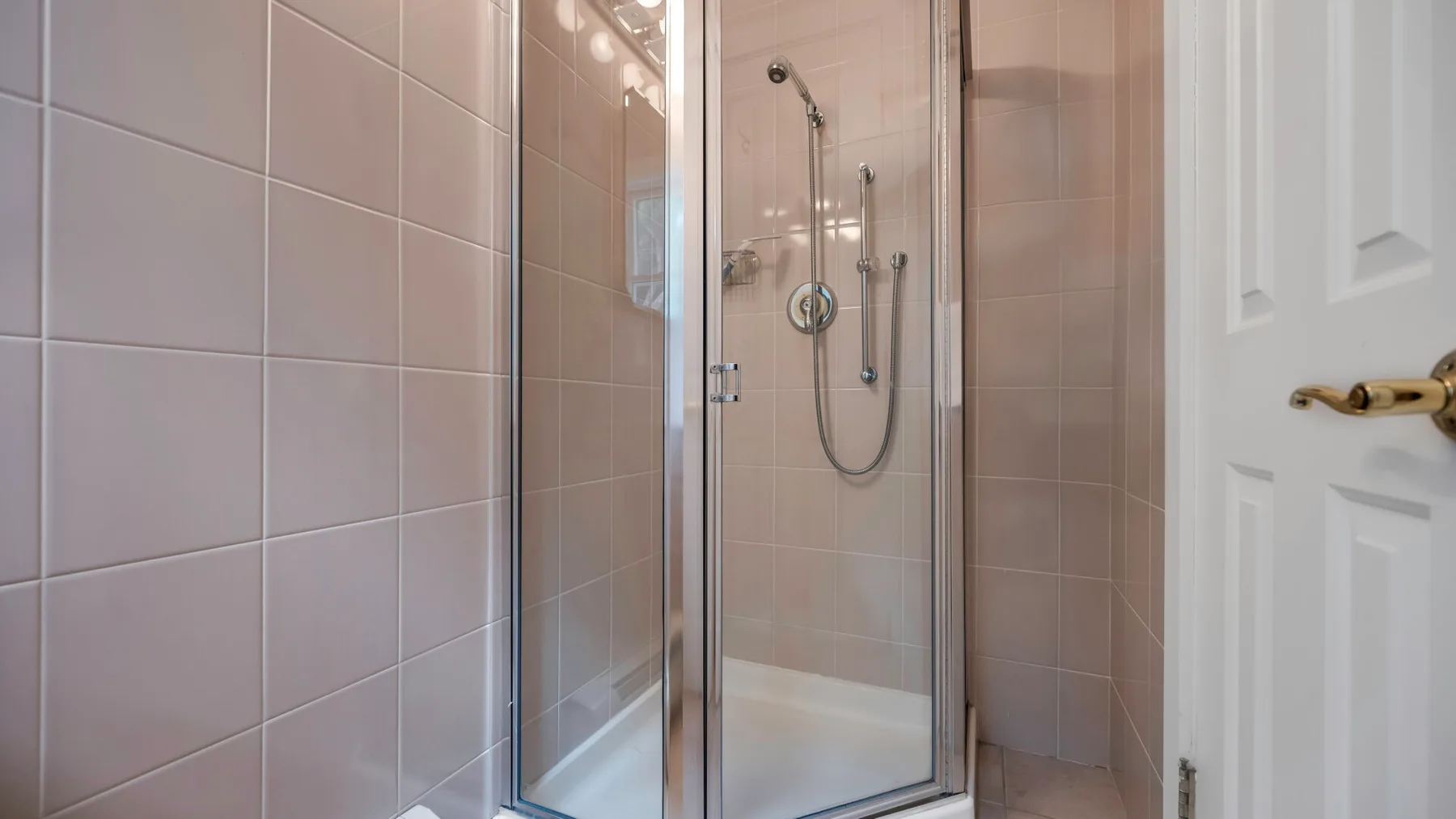 A tiled bathroom with a glass-enclosed shower beside a white door.