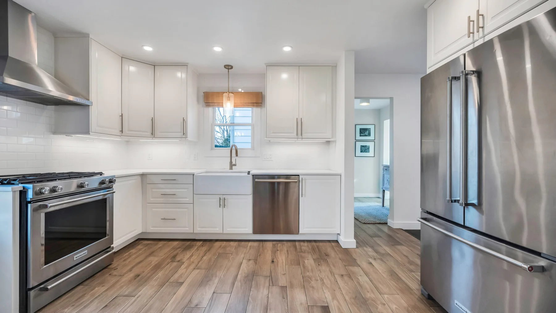 A bright kitchen with white cabinets, stainless steel appliances, and wood-look flooring.