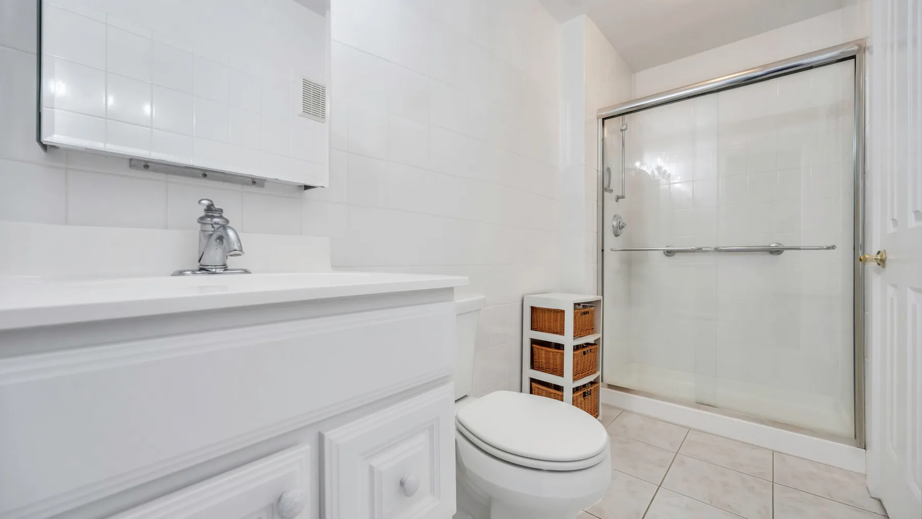 A tiled bathroom with a vanity, toilet, and glass shower.