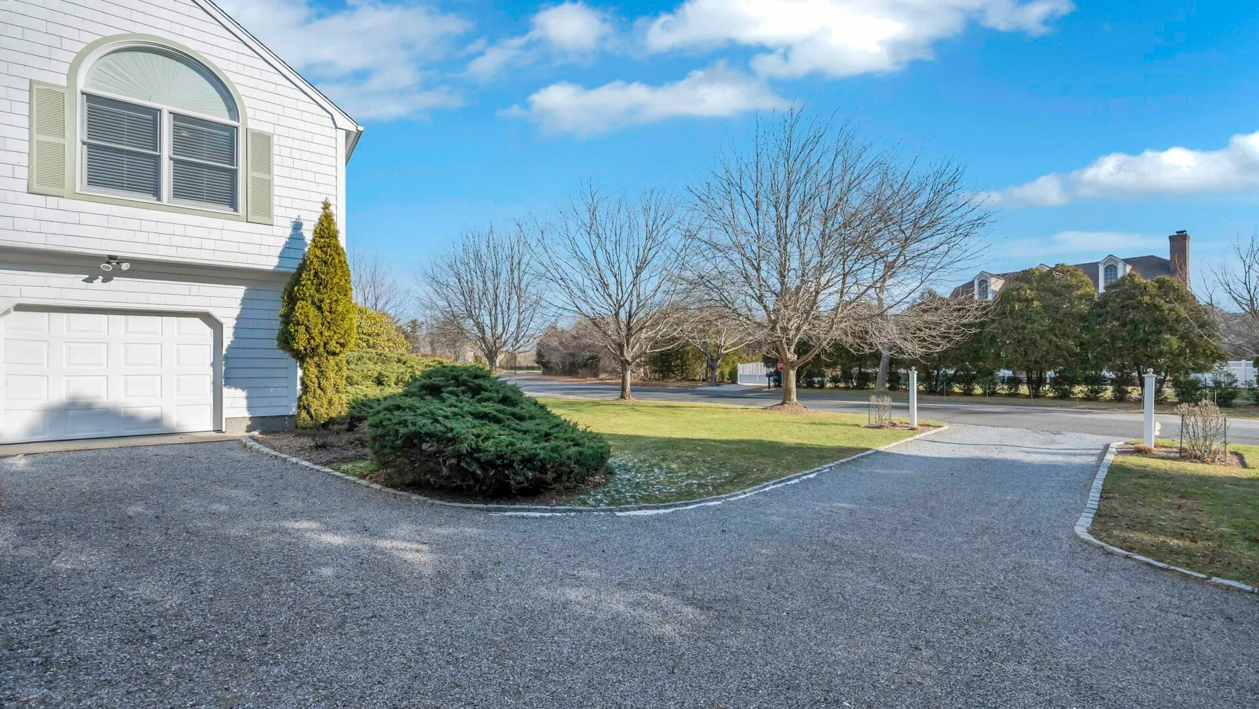A paved driveway curves past a house, shrubs, and leafless trees.