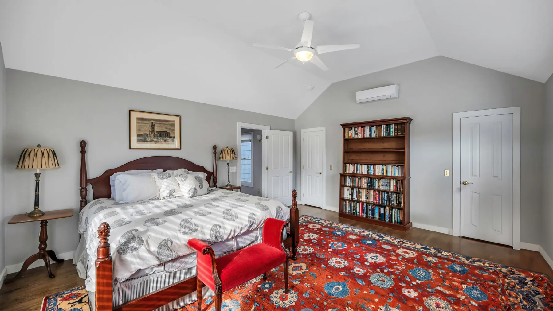 A bedroom with a large bed, a colorful rug, and a bookcase.