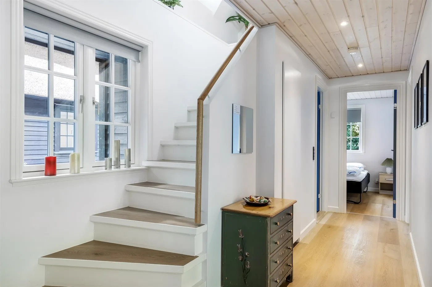 Un pasillo luminoso con una escalera y una puerta abierta a un dormitorio.