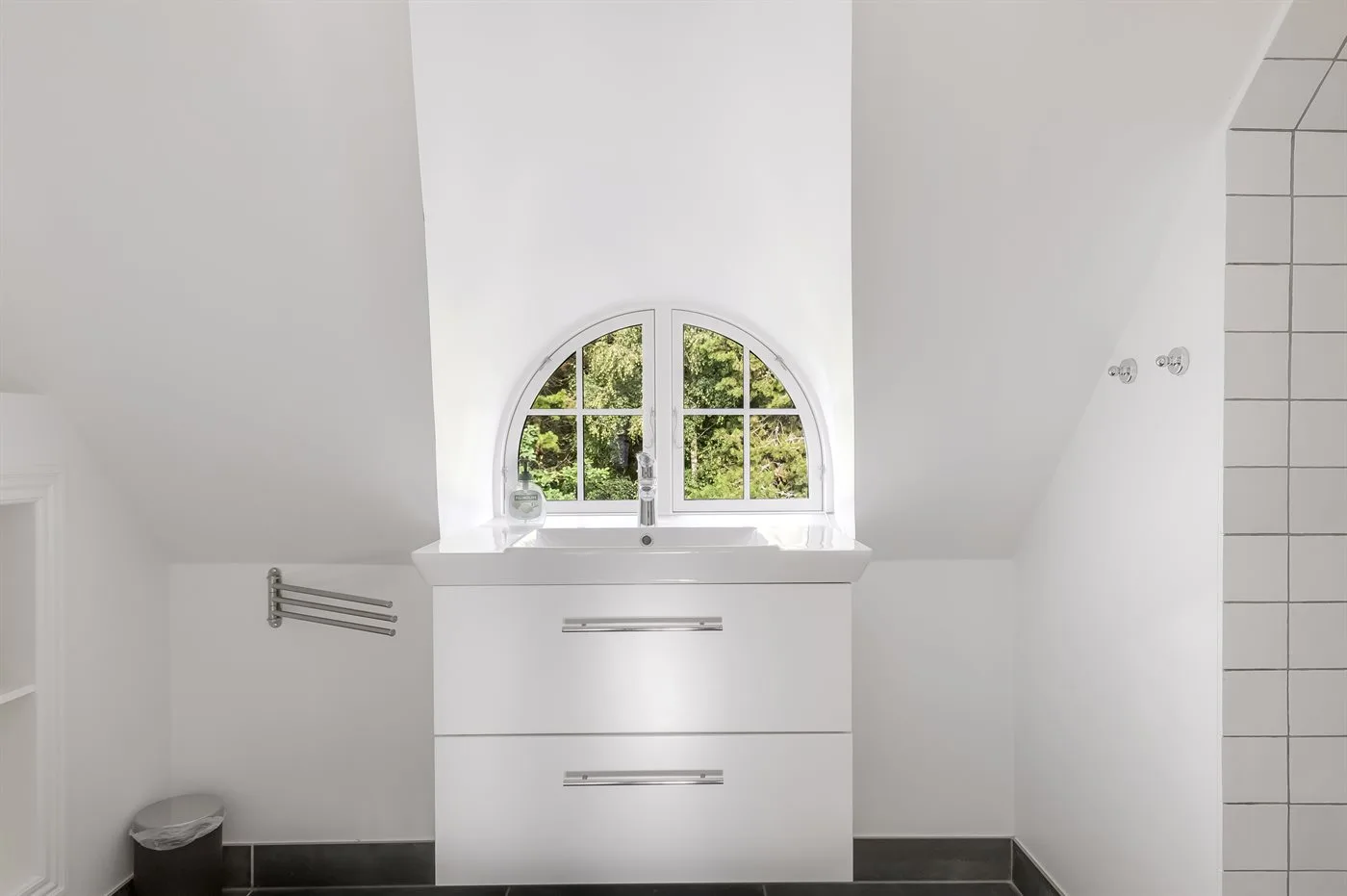 Un baño luminoso con una ventana redondeada sobre un mueble de lavabo.