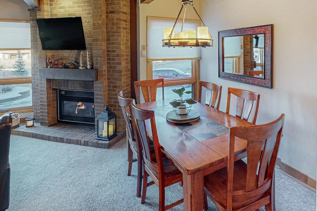 A dining area with a wooden table and chairs beside a brick fireplace.