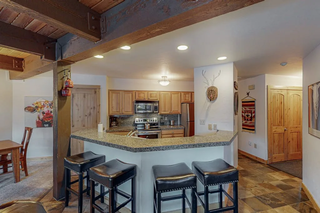 A kitchen with a curved counter and bar seating beneath exposed wooden beams.