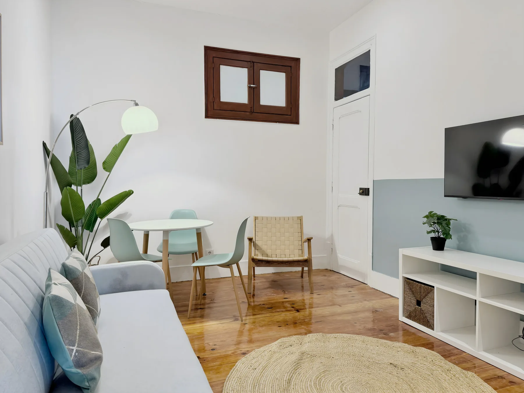 A bright living room with seating, a small dining table, and a television.