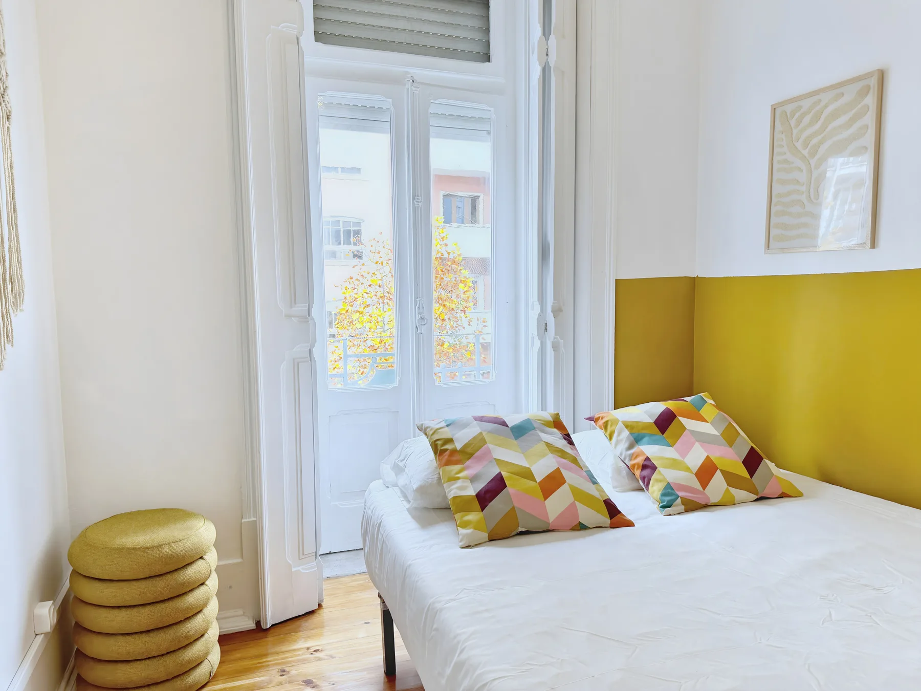 A bright bedroom with a white bed and colorful patterned pillows.