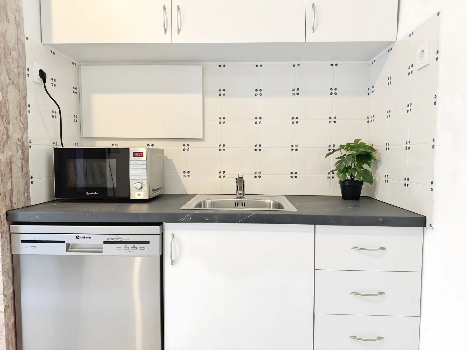 A compact kitchen with white cabinets, a countertop, and a small potted plant.