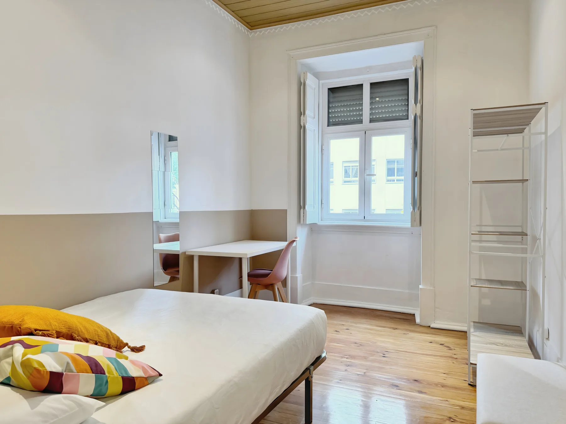 A bedroom with a bed, desk, and tall window.