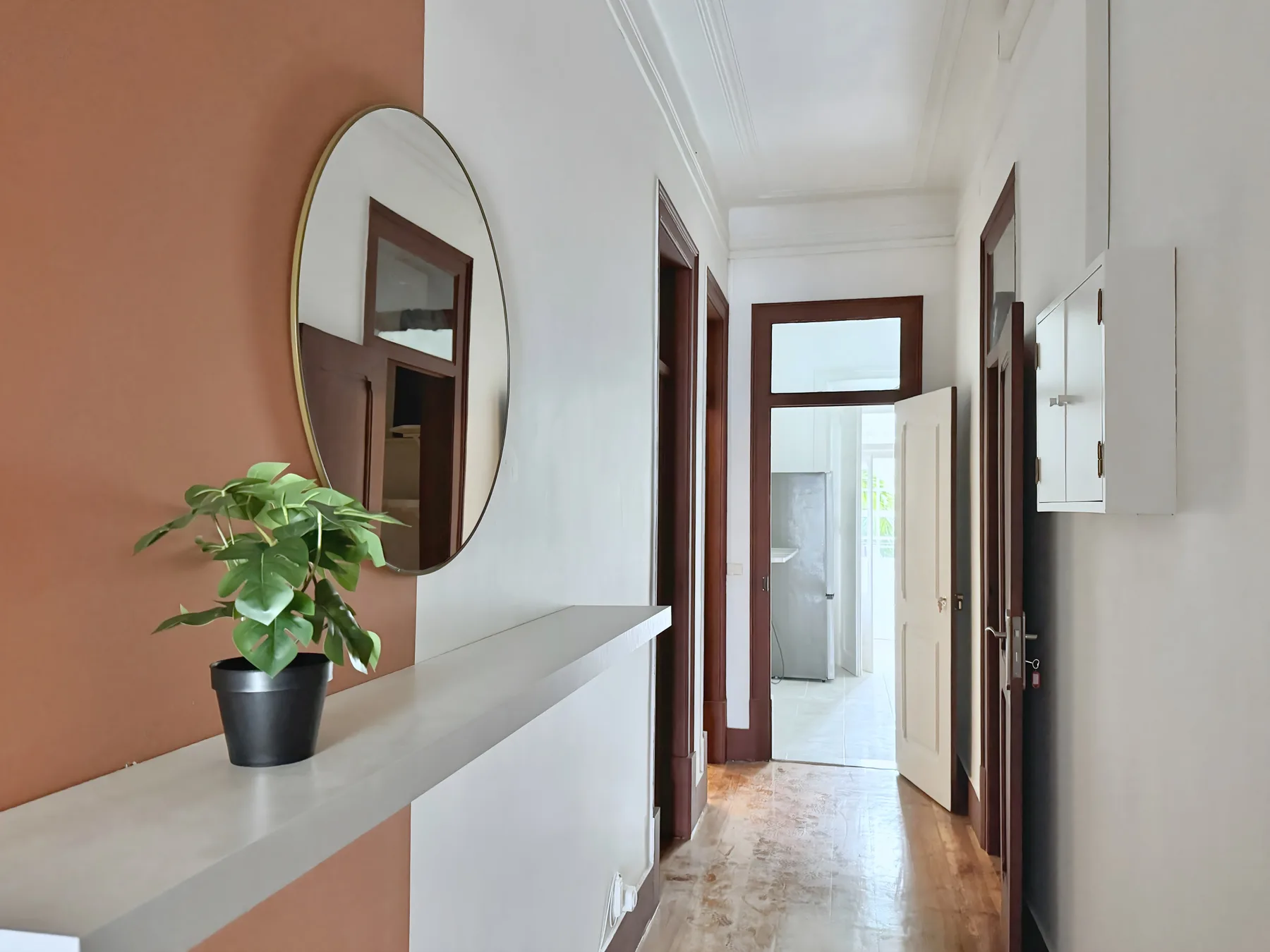 A bright hallway with a console shelf, round mirror, and potted plant.