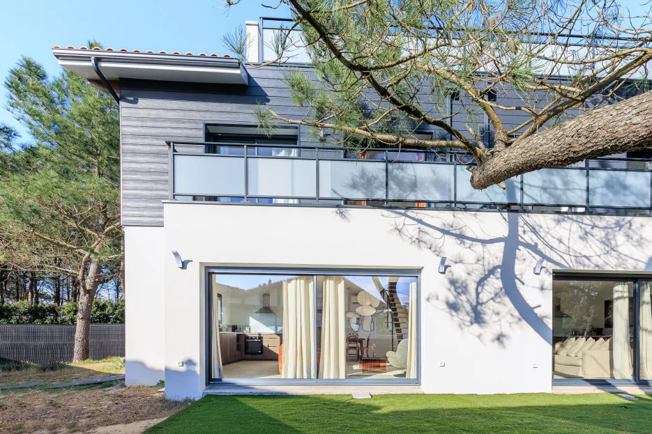 A modern house exterior with large ground-floor windows and a balcony.