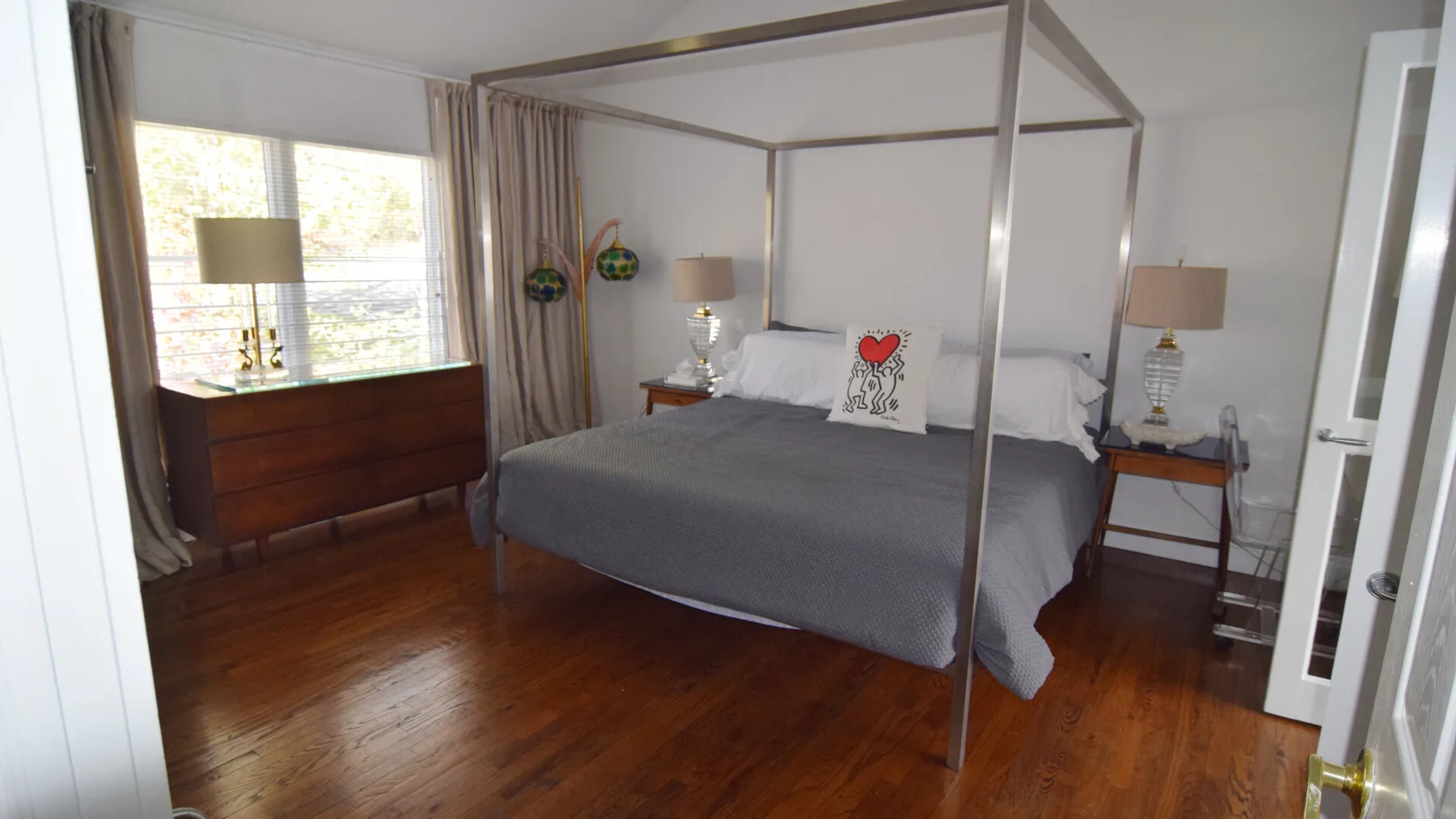 Un dormitorio con una cama con dosel, una cómoda de madera y una ventana grande.