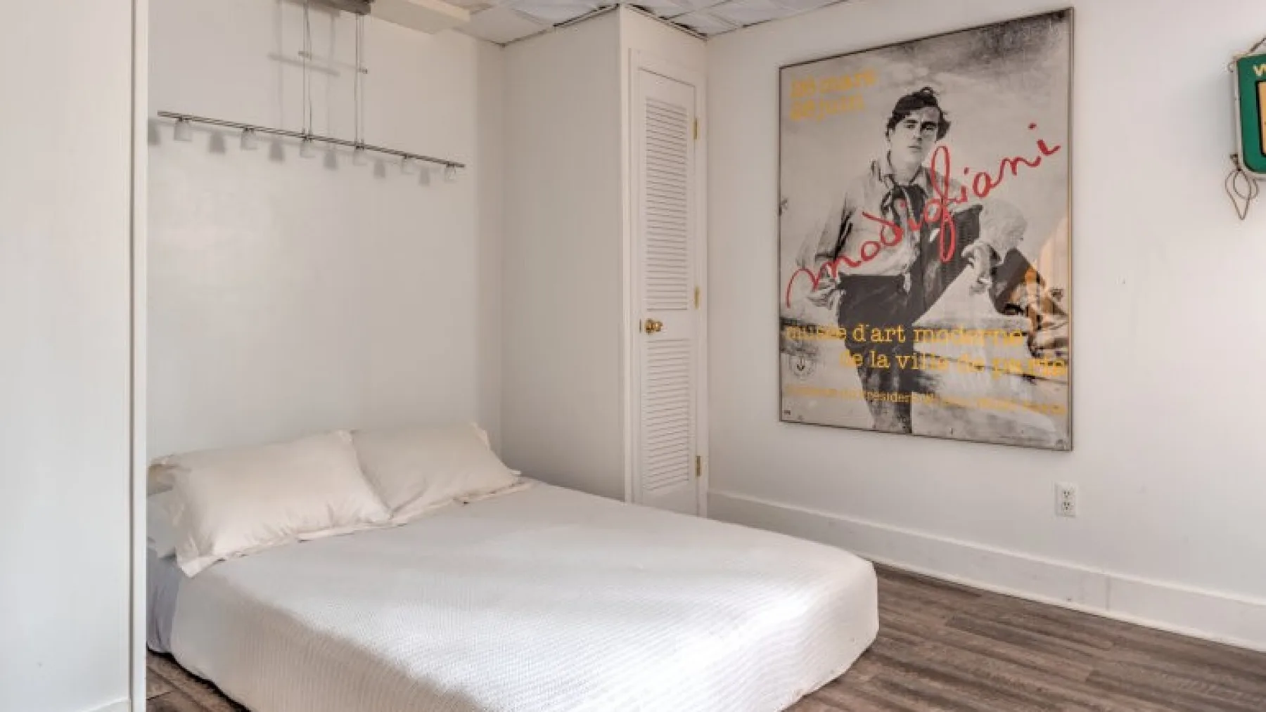 Un dormitorio con una cama bajo estantes de pared y un cartel grande.