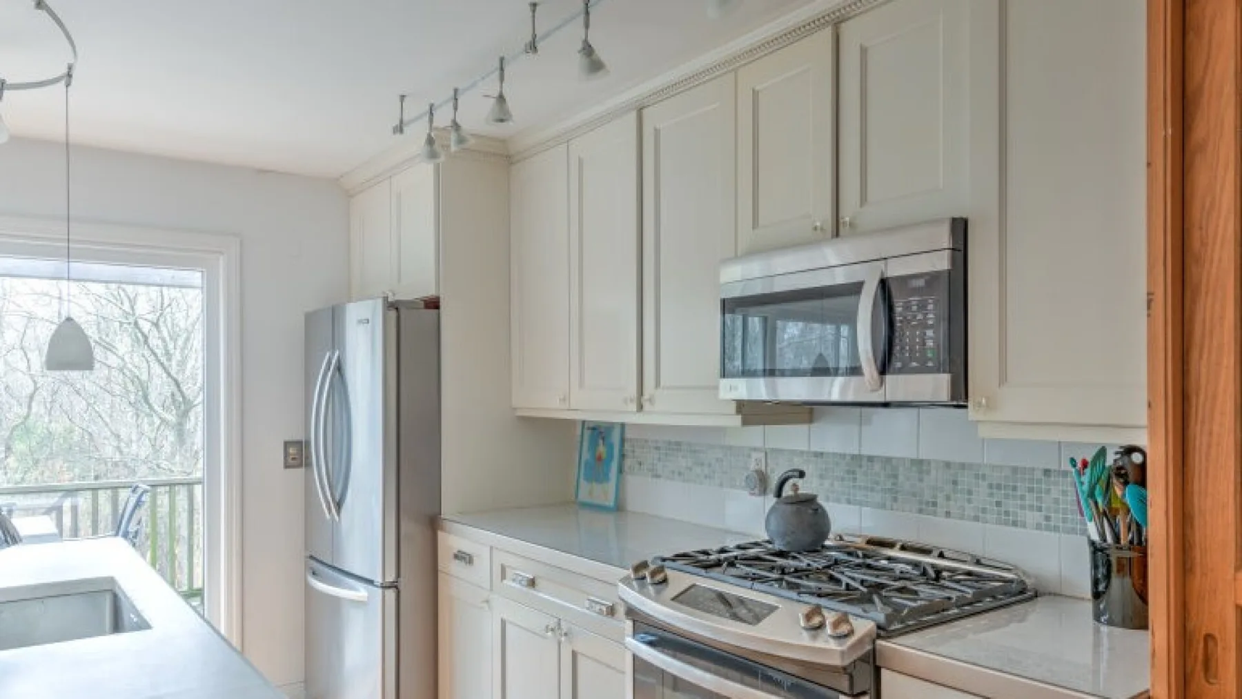Una cocina luminosa con gabinetes blancos, electrodomésticos de acero inoxidable y un salpicadero de azulejos.